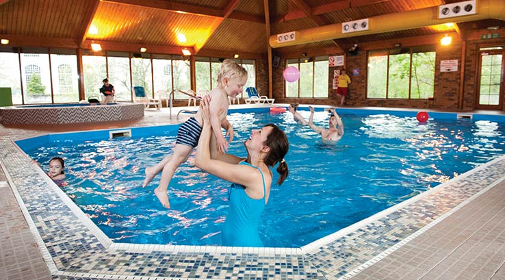 mother holding up a young boy in the indoor swimming pool