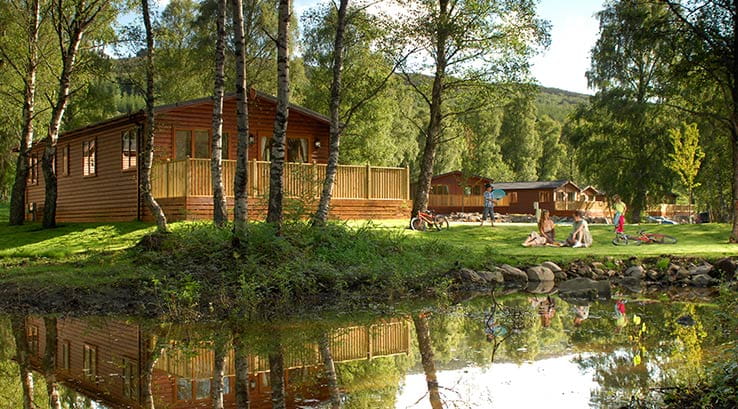 Families relaxing by the wooden lodges next to the lake at Tummel Valley Holiday Park