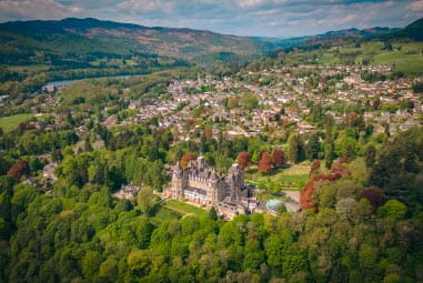 Arial view of town amongst woodland, green hills and a Blair castle