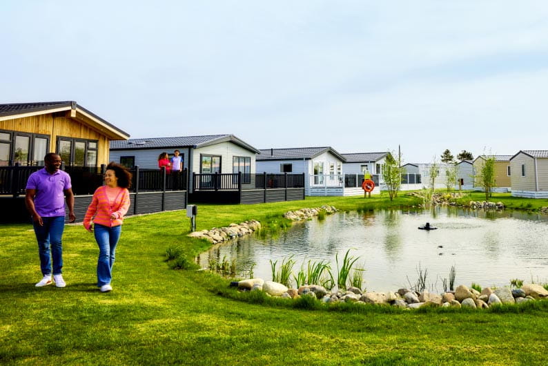Couple walking through a holiday park, past a pond