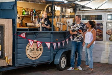 Couple with drinks at a food truck with "Y Bar Bach" logo