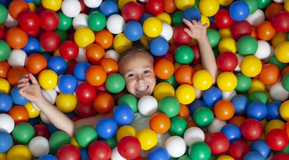 child smiling from a soft play ball pit