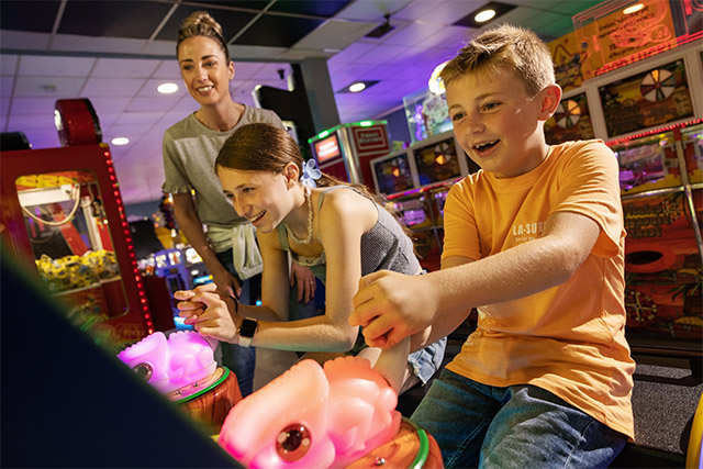 A boy and girl playing on the arcades as dad watches at Wemyss Bay Holiday Park