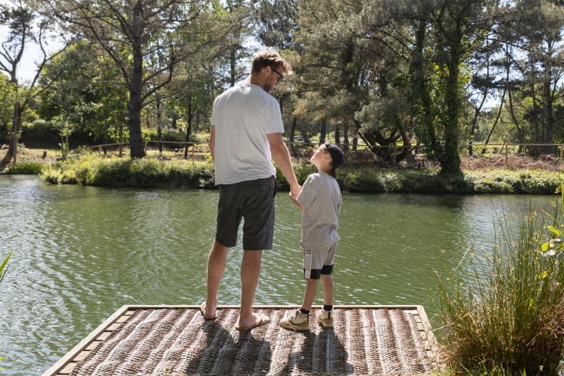 father and son standing on a jetty by a lake