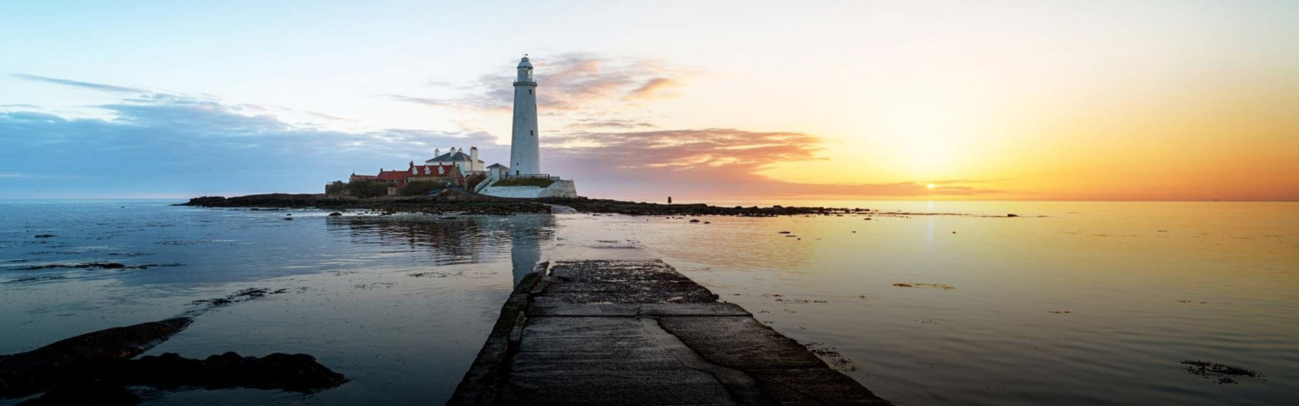 A panoramic view of the sea with a lighthouse and the sun setting