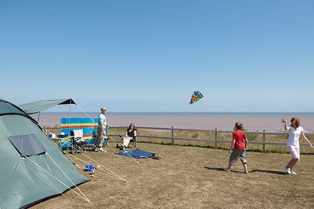 Kids flying a kite in front of their tent overlooking the sea at Withernsea Holiday Park