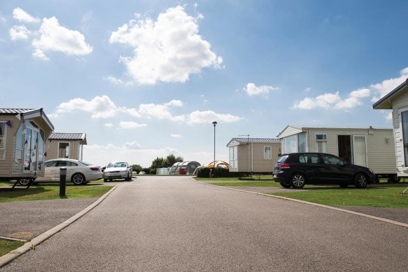 Holiday park caravans with cars parked outside either side of a paved road