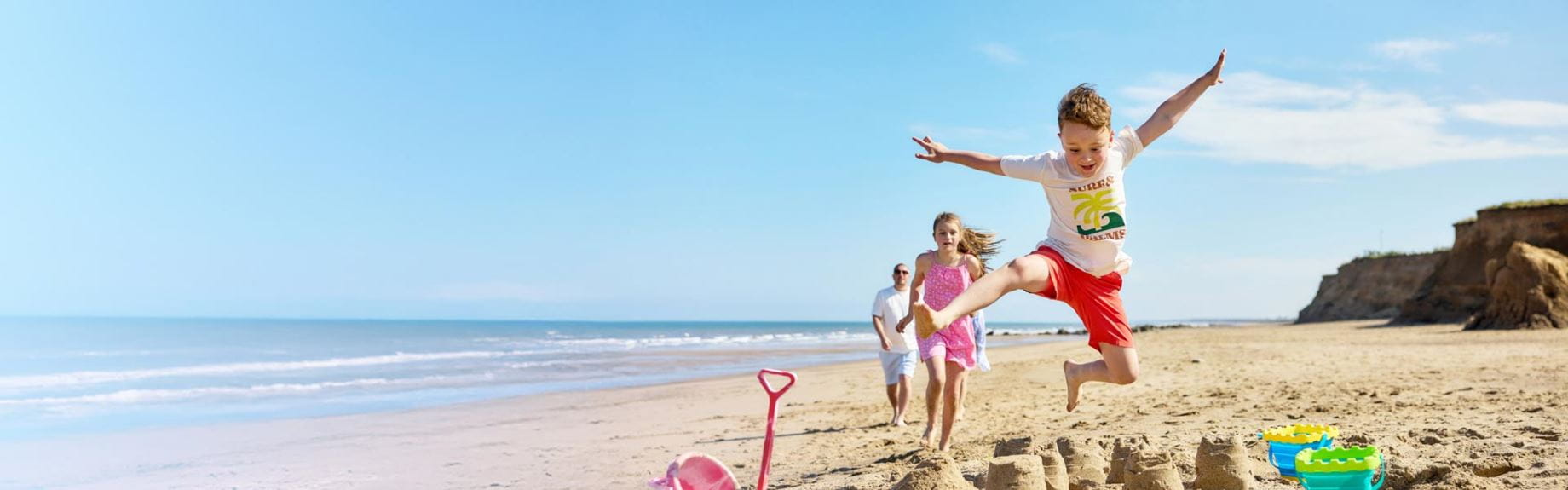 Boy jumping over sandcastle on the beach