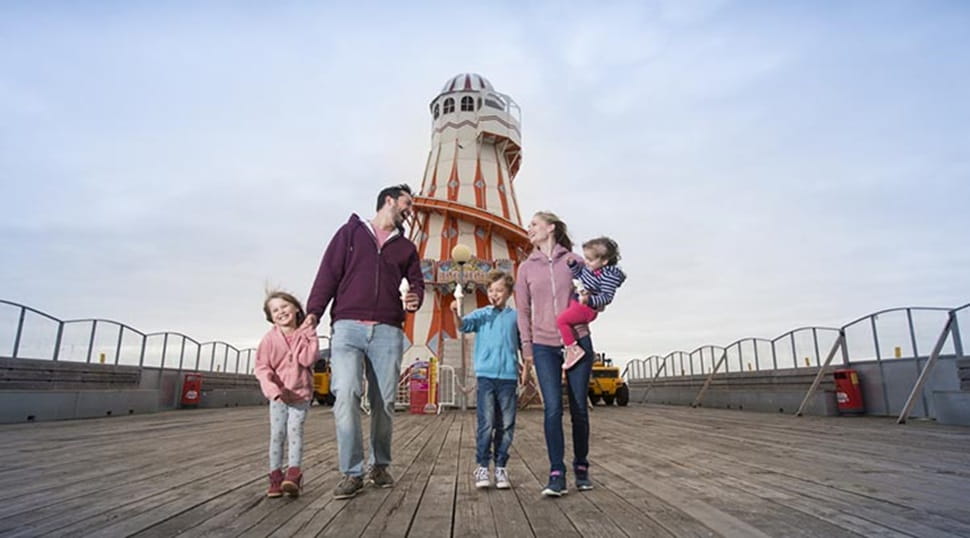 A family walking along Clacton Pier with the helter skelter in the background