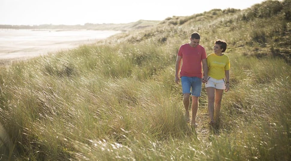 A couple walking through the grassy sand dunes of a Northumberland beach