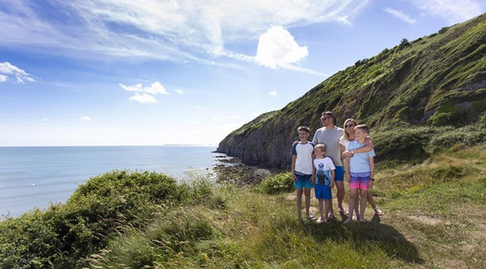 A family standing on a grassy clifftop overlooking the sea