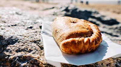 A Cornish pasty resting on a napkin on a rock by the beach