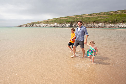 A family wading through the water at low tide at Crantock Beach
