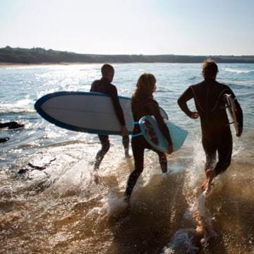 Family walking into the sea holding surfboards