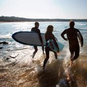 Family walking into the sea holding surfboards