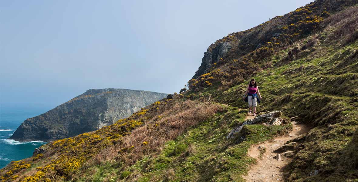 A woman walking along a coastal path in Cornwall