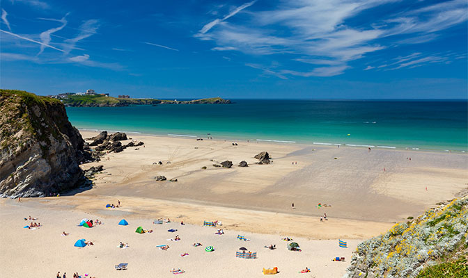 A sandy beach with clear blue waters looking across the bay to Newquay in Cornwall