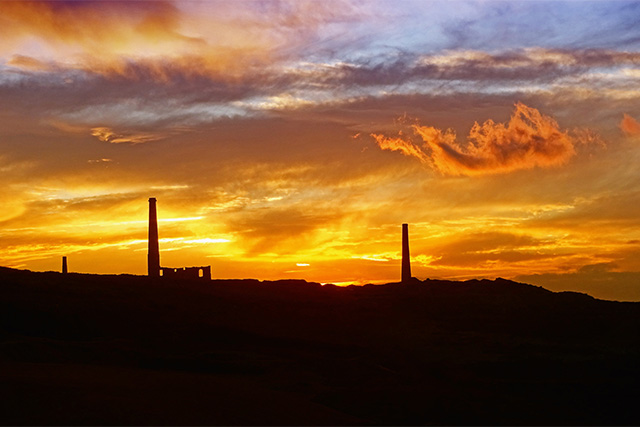 Chimneys and buildings from historic tin mines silhouetted against the sunset in Cornwall
