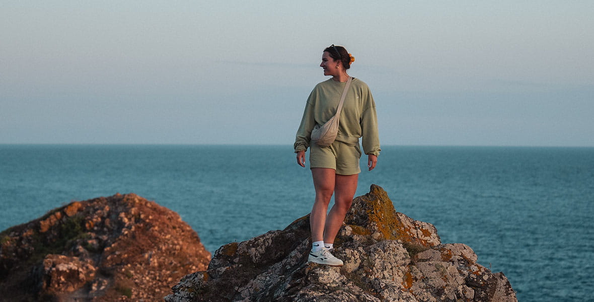 A girl climbing a rocky viewpoint on the Cornish coast at sunset