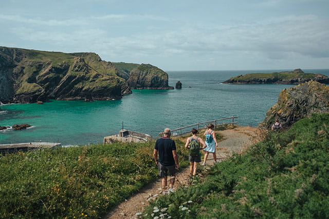 A family walking along a coastal path overlooking a bay in Cornwall