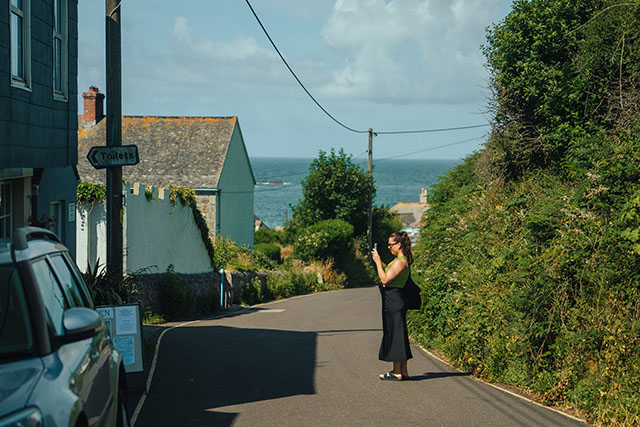 A tourist taking a photo outside a shop in a Cornish seaside village