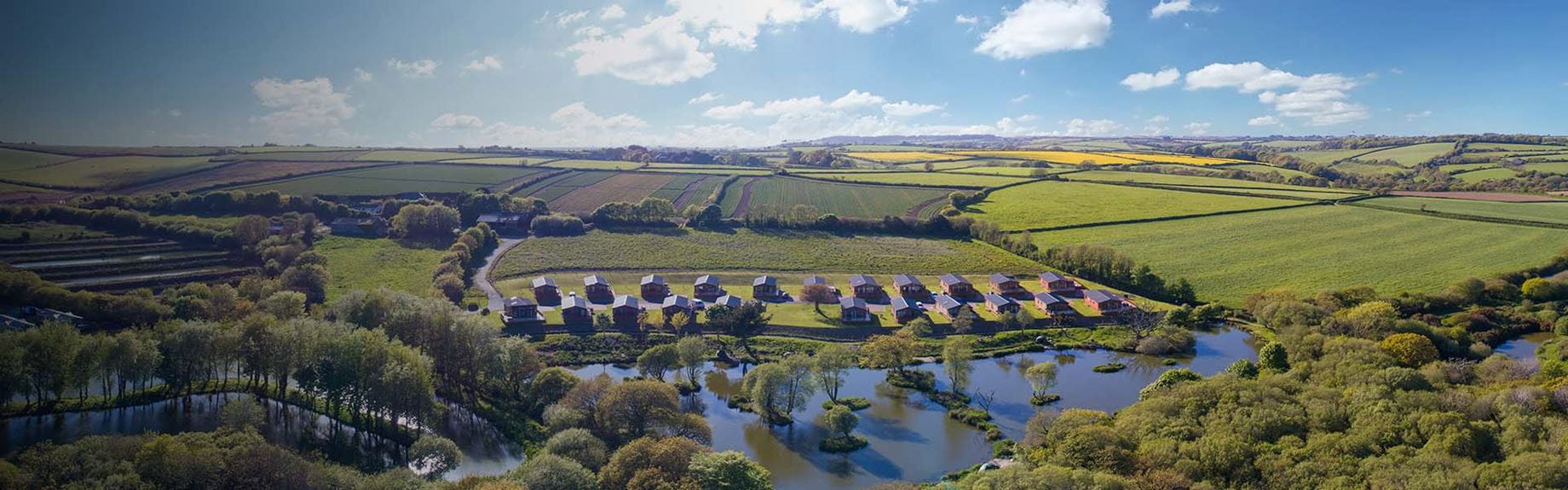 An aerial view of lodges in the Cornish countryside, overlooking at lake at White Acres Holiday Park