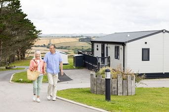 A couple walking past their holiday home lodge in Cornwall