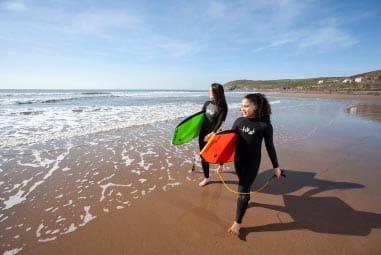 Kids walking on the sand holding surfboards