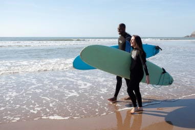 Couple walking on the beach holding surfboards