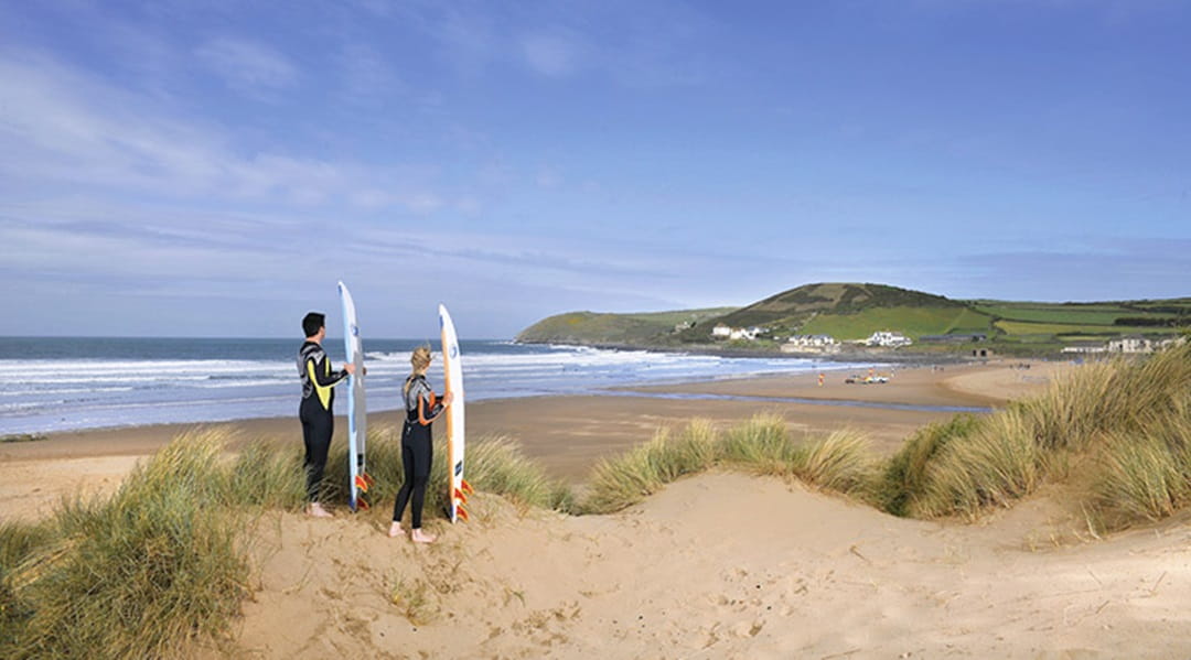 couple with surfboards looking over the beach to the sea