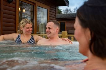 Friends laughing in a hot tub outside their holiday lodge