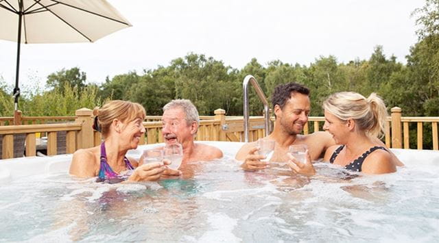 two couples laughing and drinking wine in a hot tub