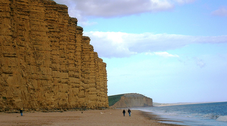 Large vertical, sand coloured cliffs next to the sea