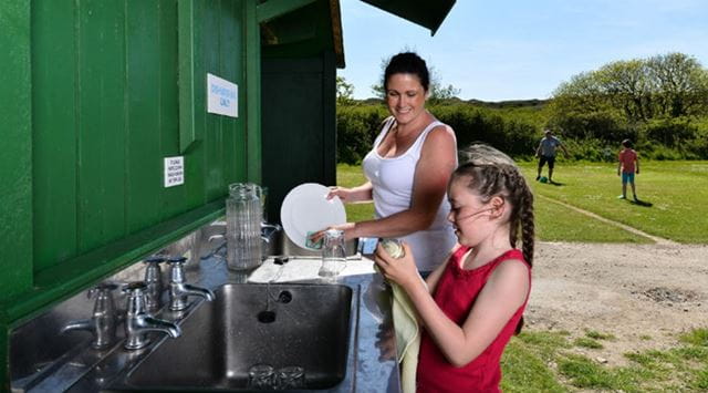 mother and daughter wash dishes on a campsite utility area
