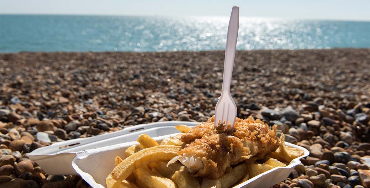 A takeaway box of fish and chips sitting on the beach