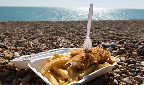 A takeaway box of fish and chips sitting on the beach