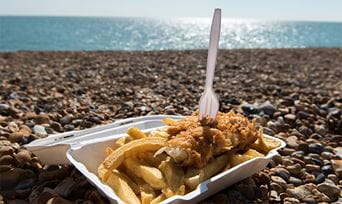 A takeaway box of fish and chips sitting on the beach