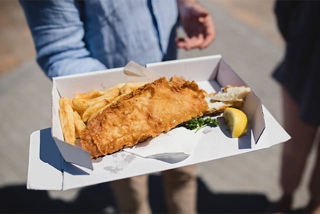 A person holding a cardboard box of fish and chips