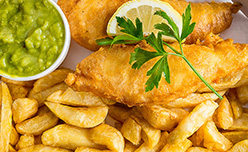 A close-up of a plate of fish, chips, mushy peas and a lemon wedge