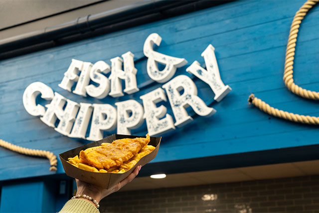 A person holding a plate of fish and chips in front of the Fish and Chippery at Vauxhall Holiday Park in Norfolk