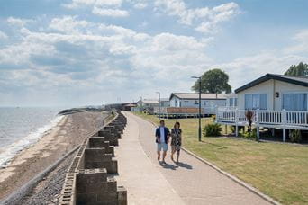 A couple walking past their holiday home lodge at Coopers Beach Holiday Park on the Essex Coast