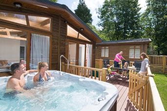 Parents relaxing in a hot tub while chatting to their grandparents and children on the veranda of their holiday lodge