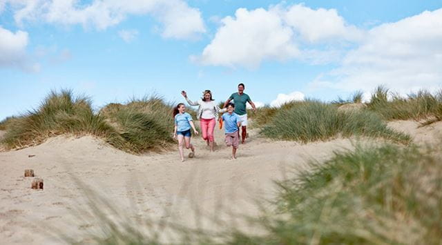 A family running to the beach through the dunes at Camber Sands in Sussex