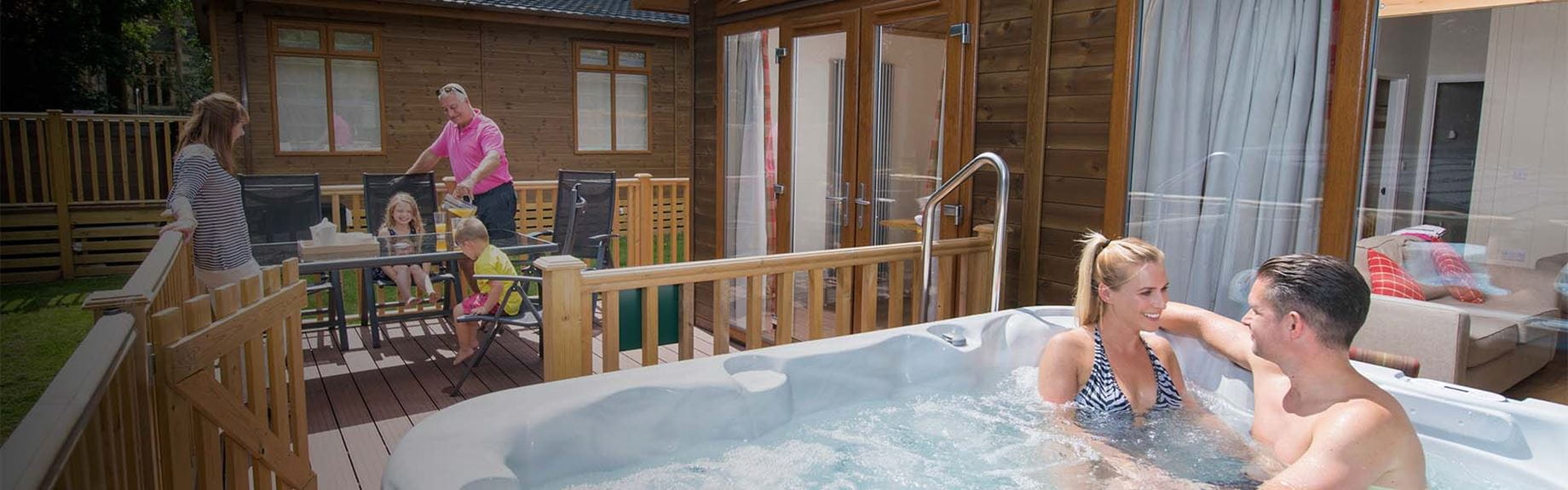 A family on the veranda of their holiday lodge with a hot tub