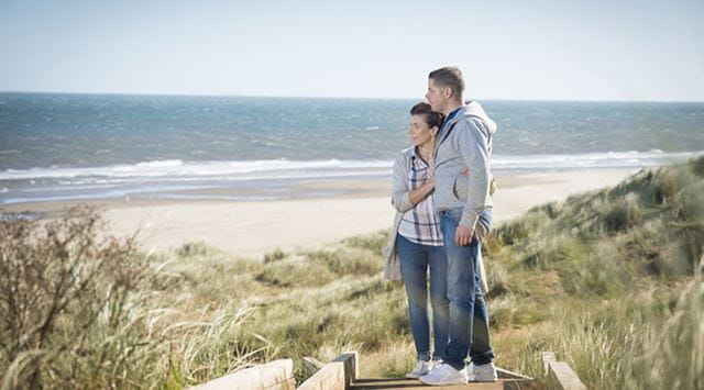 A couple enjoying the view of a beach from the dunes
