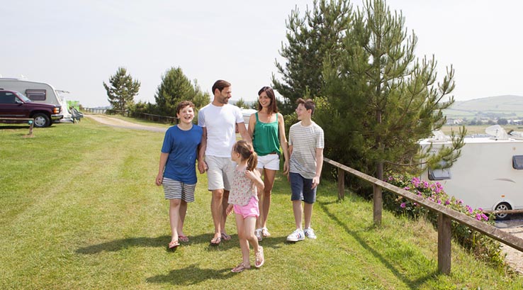 a family walking through a touring caravan field on a sunny day