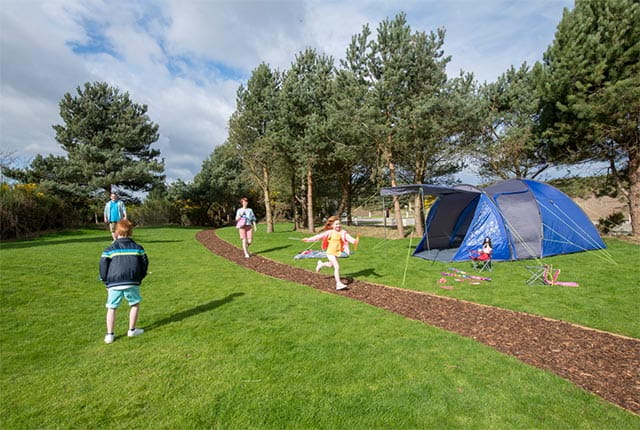 A family playing outside a tent at Nairn Lochloy Campsite