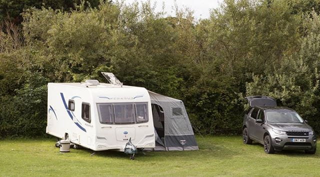 A touring caravan, awning and land rover on a grassy pitch at a Parkdean Resorts campsite in Scotland