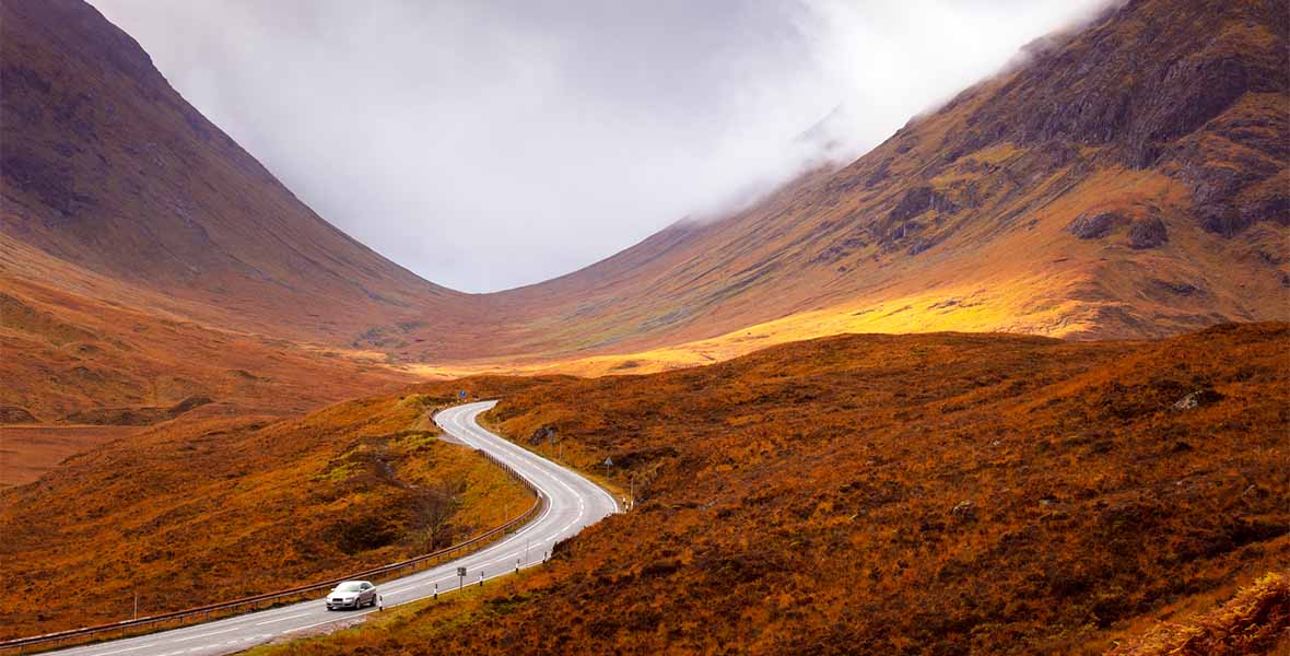 A car driving through a glen in Scotland on an autumn day