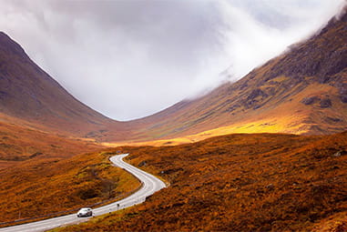 A car driving through a glen in Scotland on an autumn day
